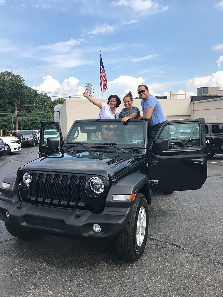 A group of people are standing next to a jeep in a parking lot.
