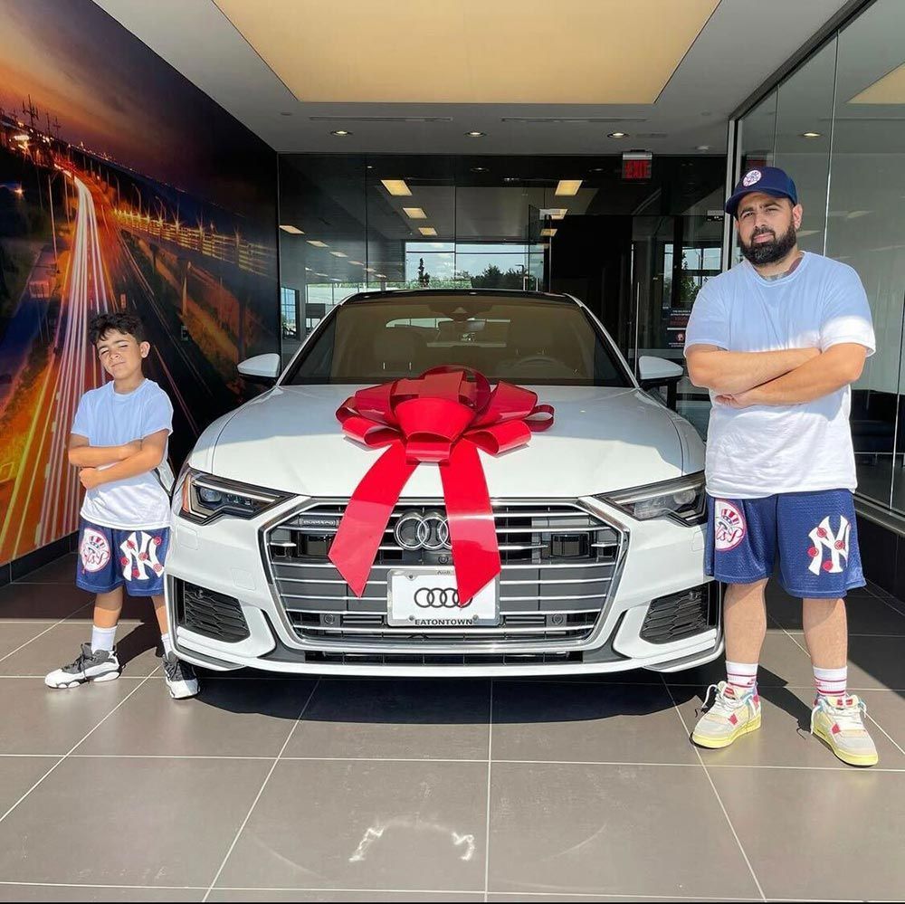 A man and a boy are standing in front of a white car with a red bow on it.