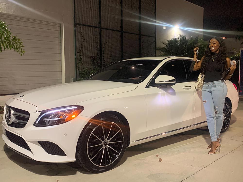 A woman is standing in front of a white mercedes benz.