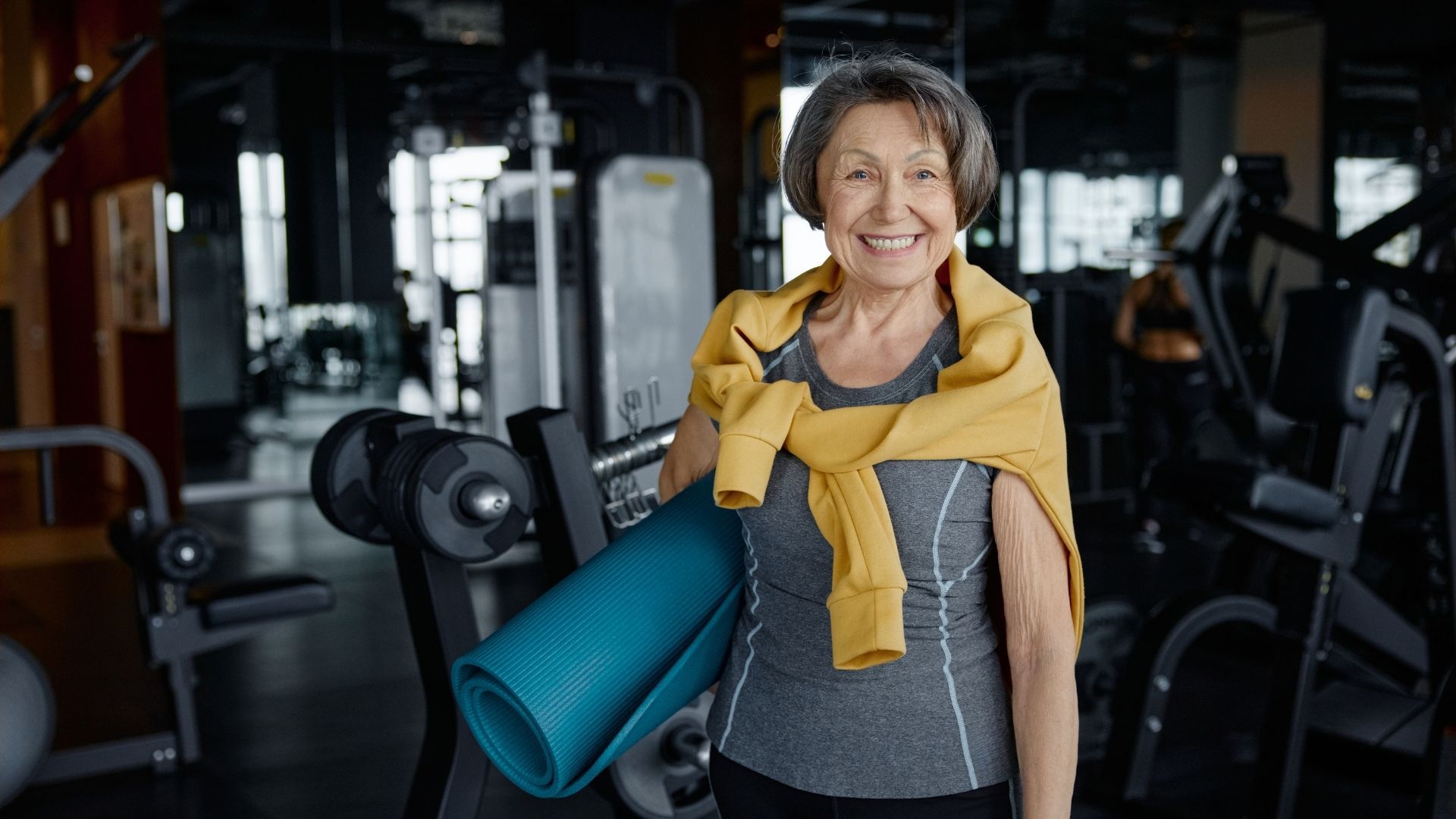Smiling woman holding a yoga mat and towel in a gym