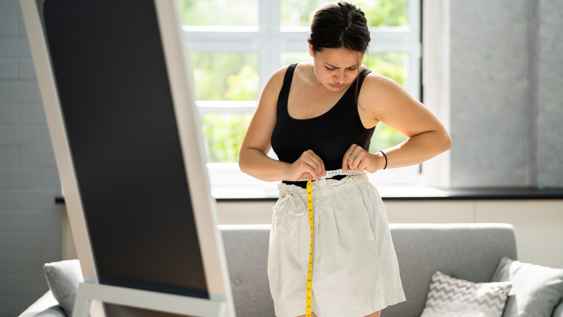 Woman measuring a white garment with a tape measure in a bright living room
