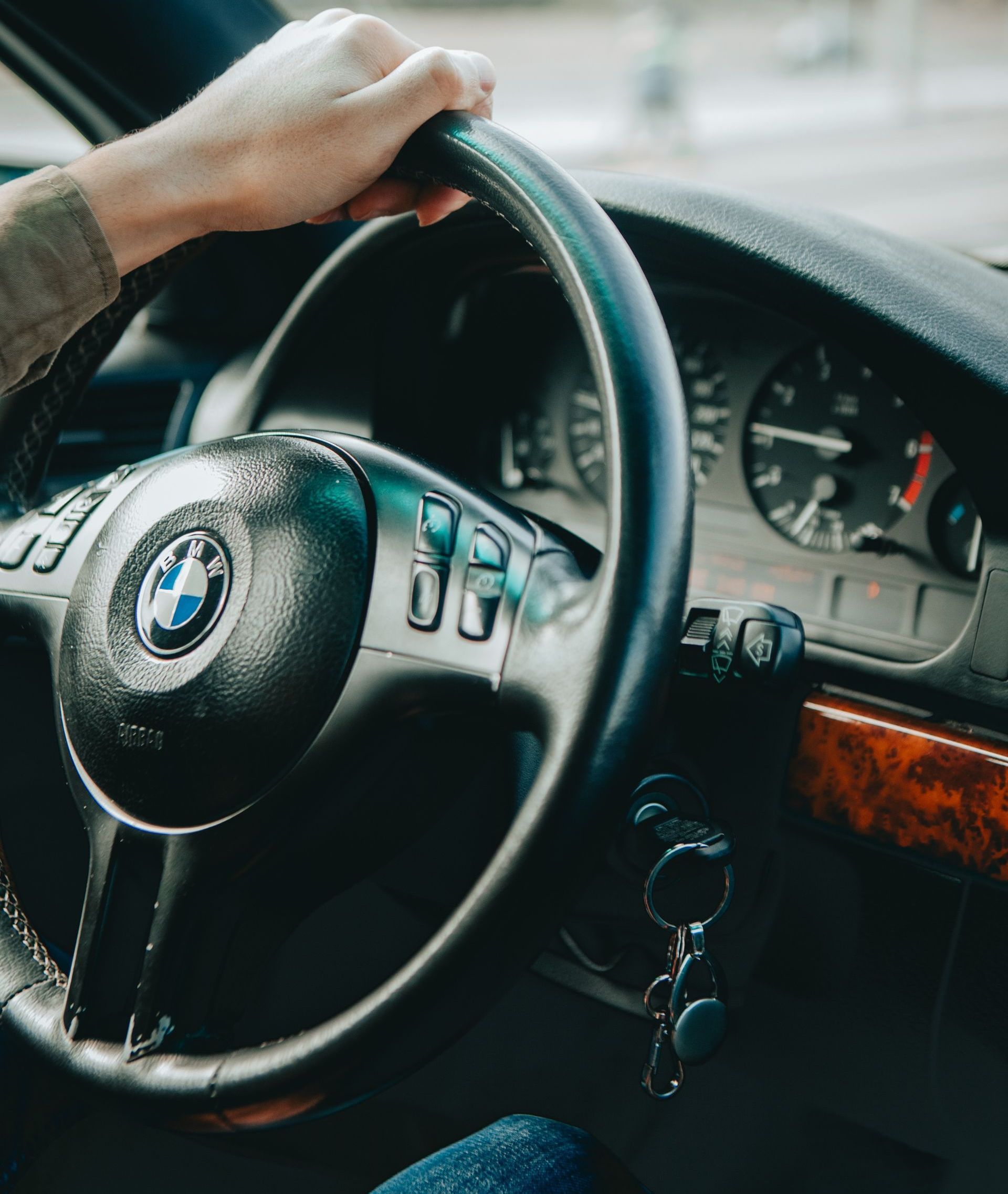 A car key inserted in the ignition while a man is driving, holding the steering wheel.