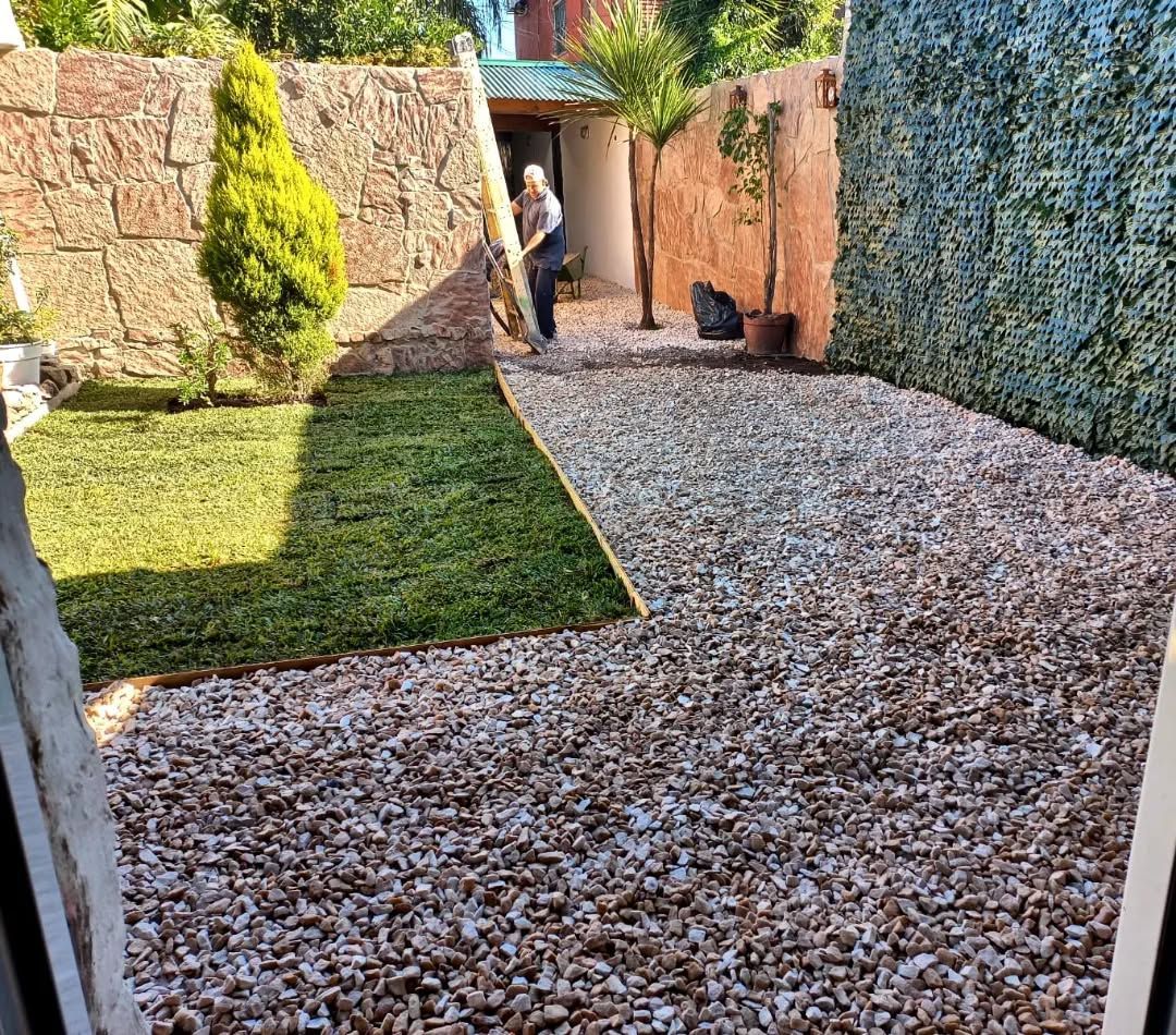 Un hombre está parado en un patio de grava al lado de un exuberante césped verde.