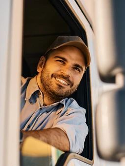 A man is sitting in the driver 's seat of a truck and smiling.
