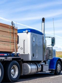 A semi truck with a trailer full of wood is parked on the side of the road.