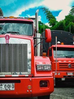 Two red semi trucks are parked next to each other in a parking lot.