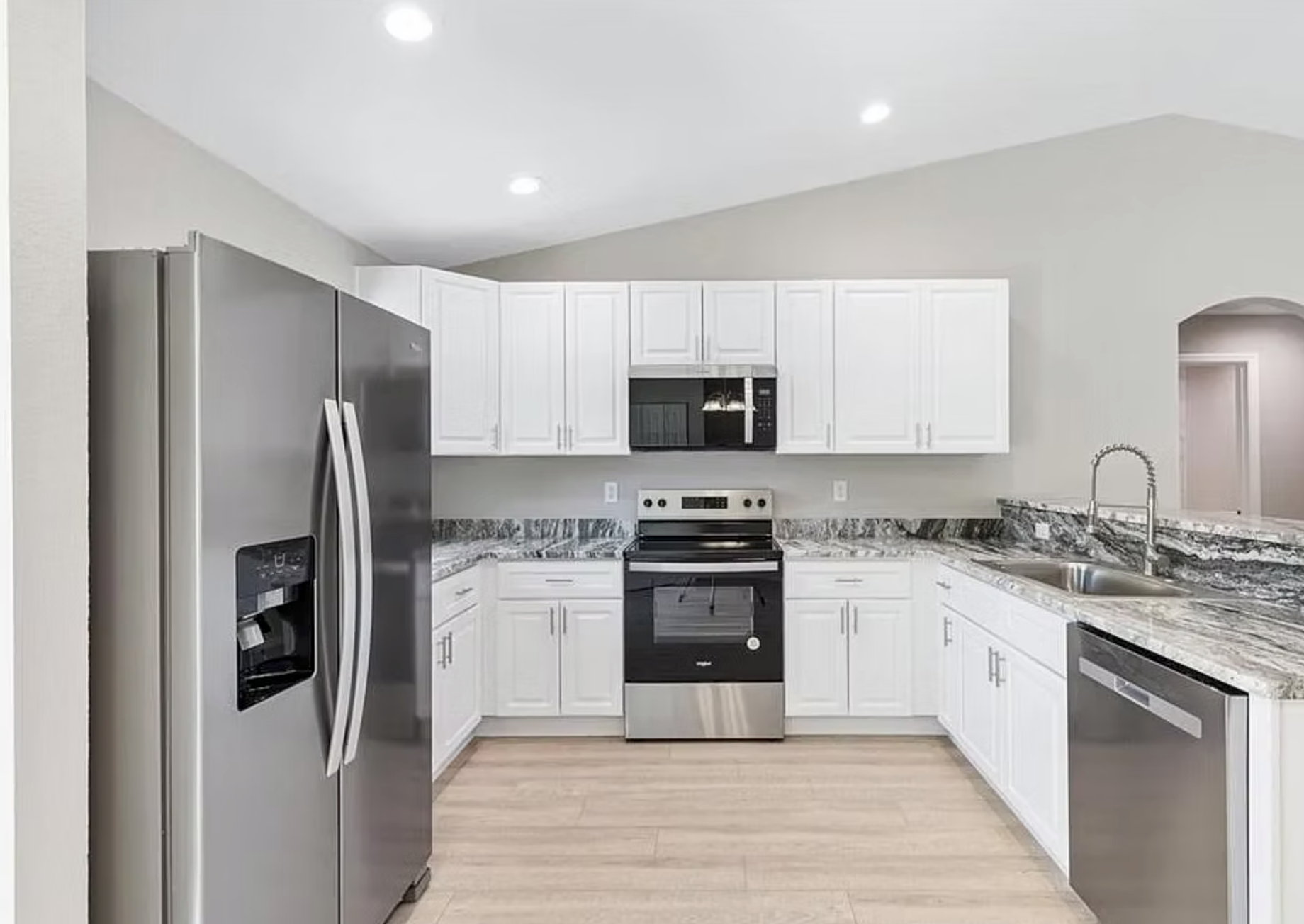 Modern white kitchen with stainless steel appliances and light wood flooring