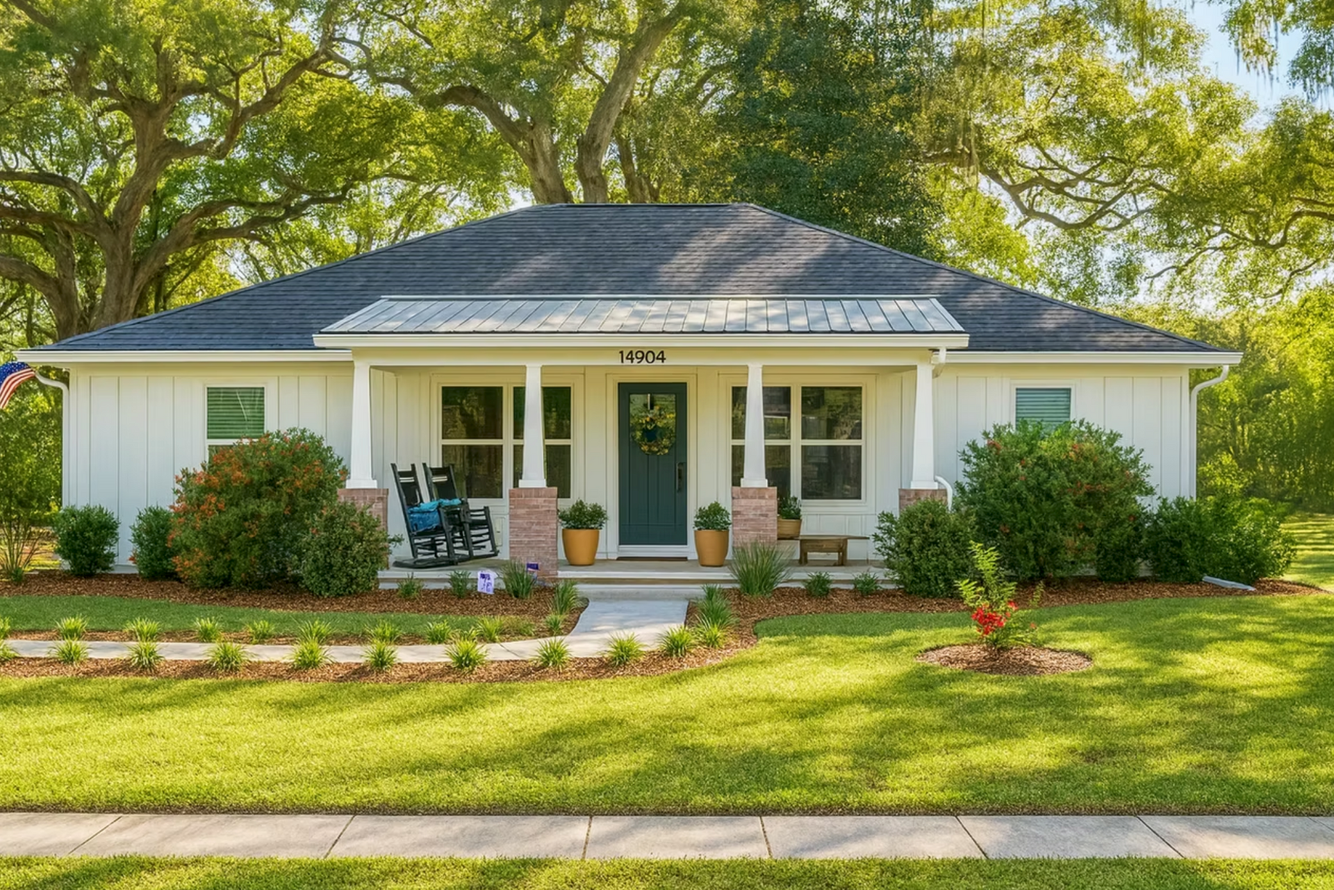 Single-story white house with gray roof, front porch, and green lawn under leafy trees