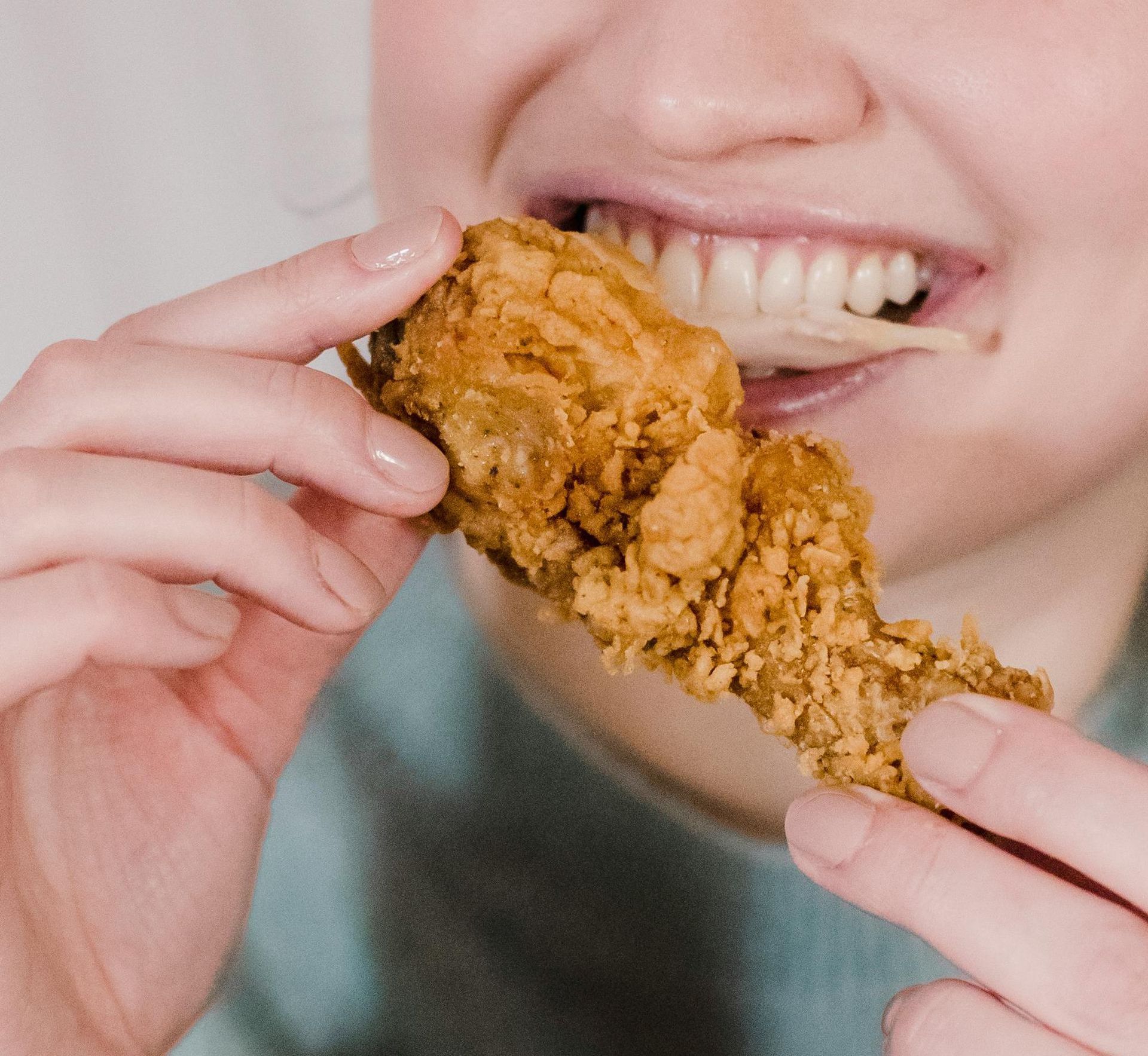 A woman is eating a piece of fried chicken.