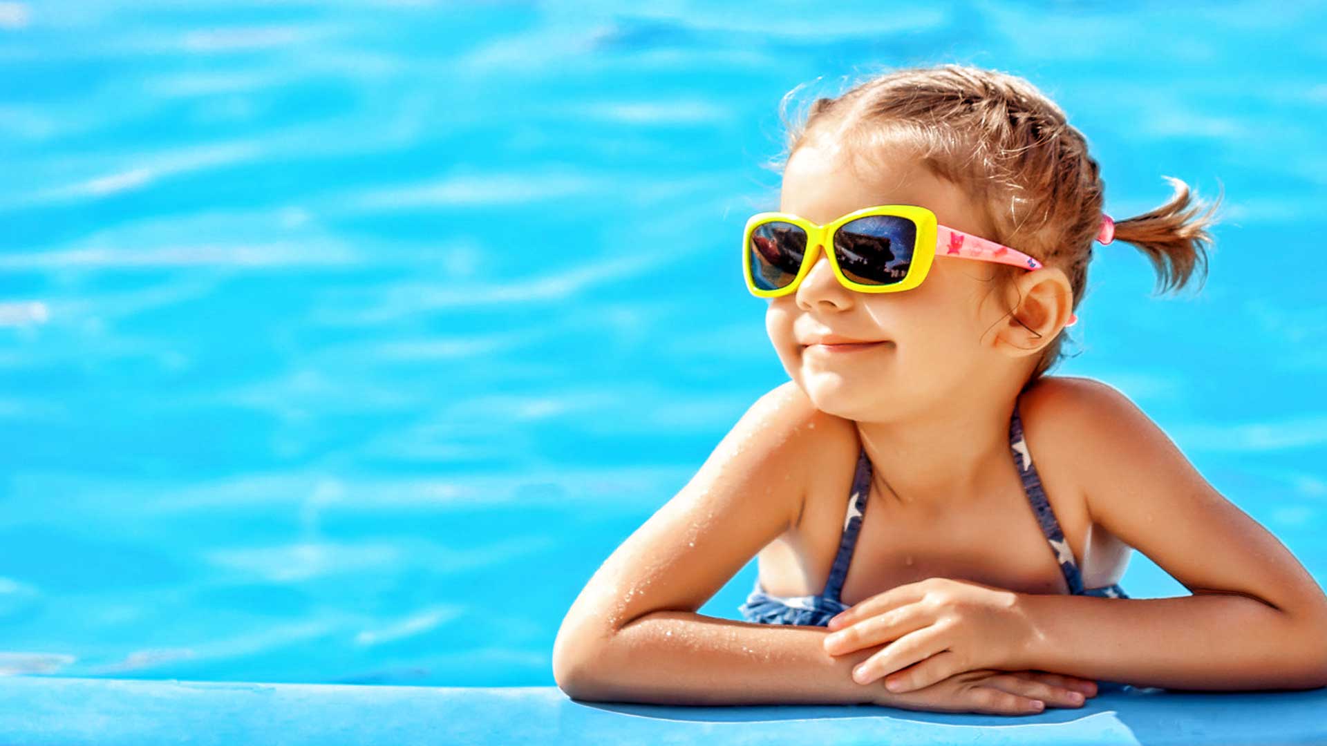 Young child wearing sunglasses smiles in a blue pool.