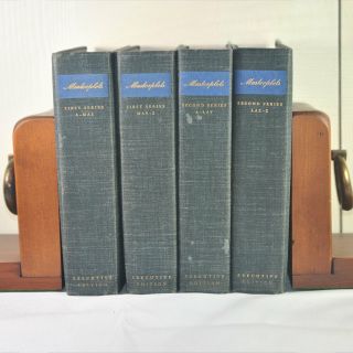 Four books are stacked on top of each other on a wooden shelf.