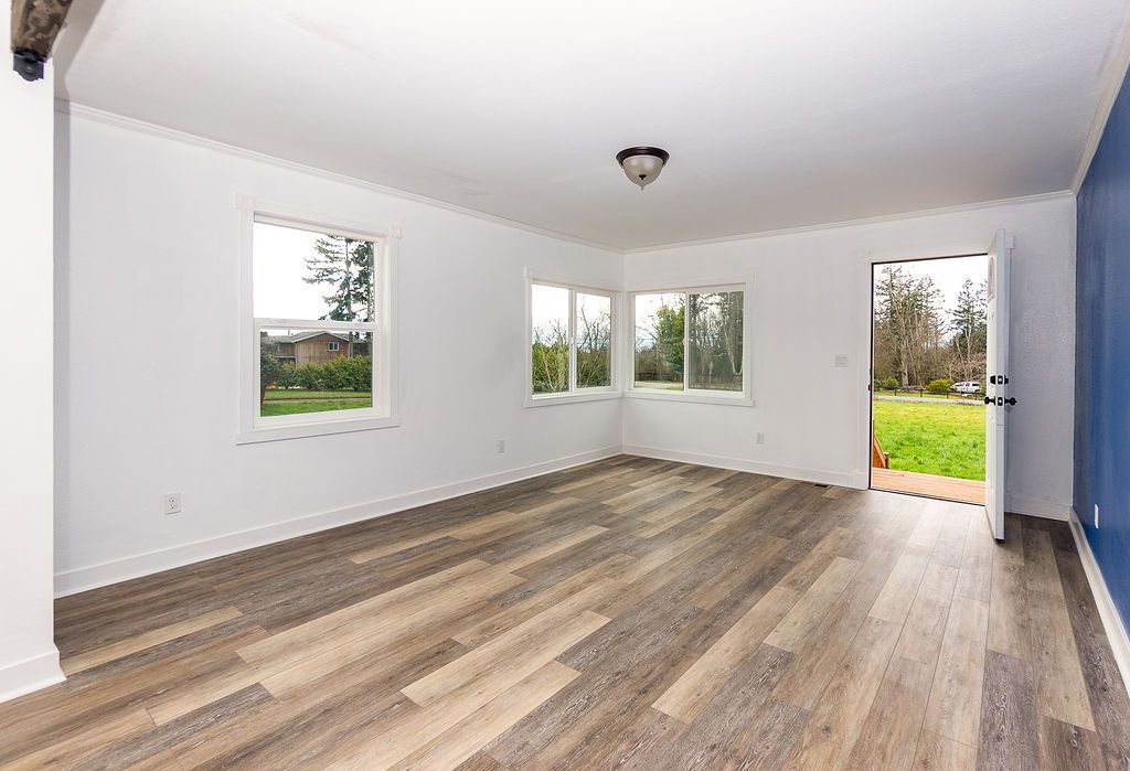 Empty room with wood-look flooring, white walls, and windows looking out onto a grassy yard.