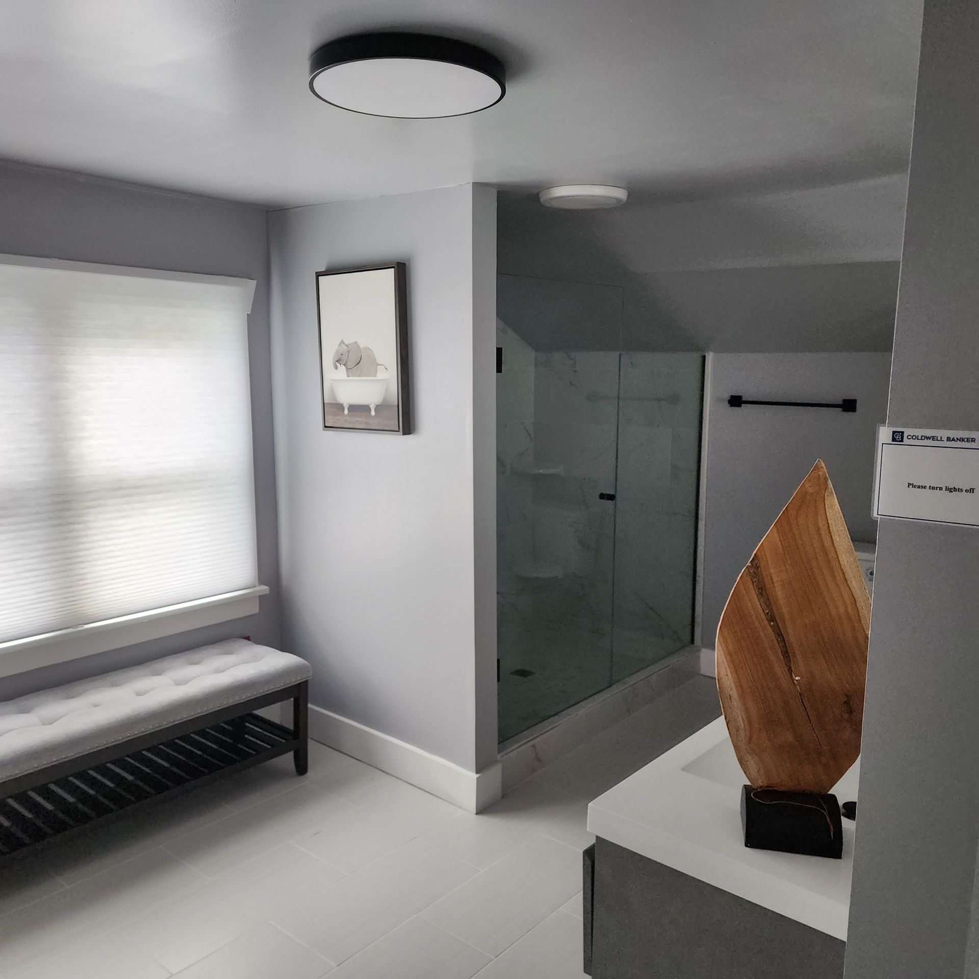 Gray bathroom with bench, art, a shower, and wooden sculpture on a countertop.