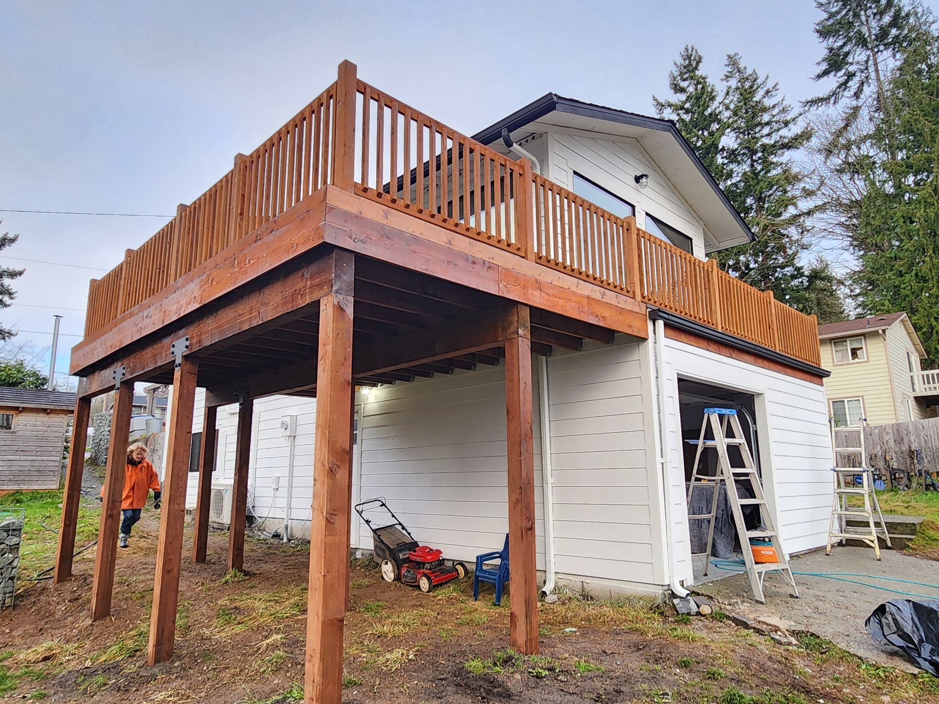 Wooden deck built above a white garage. Brown wood posts, railings, and deck surface. Person walking below.