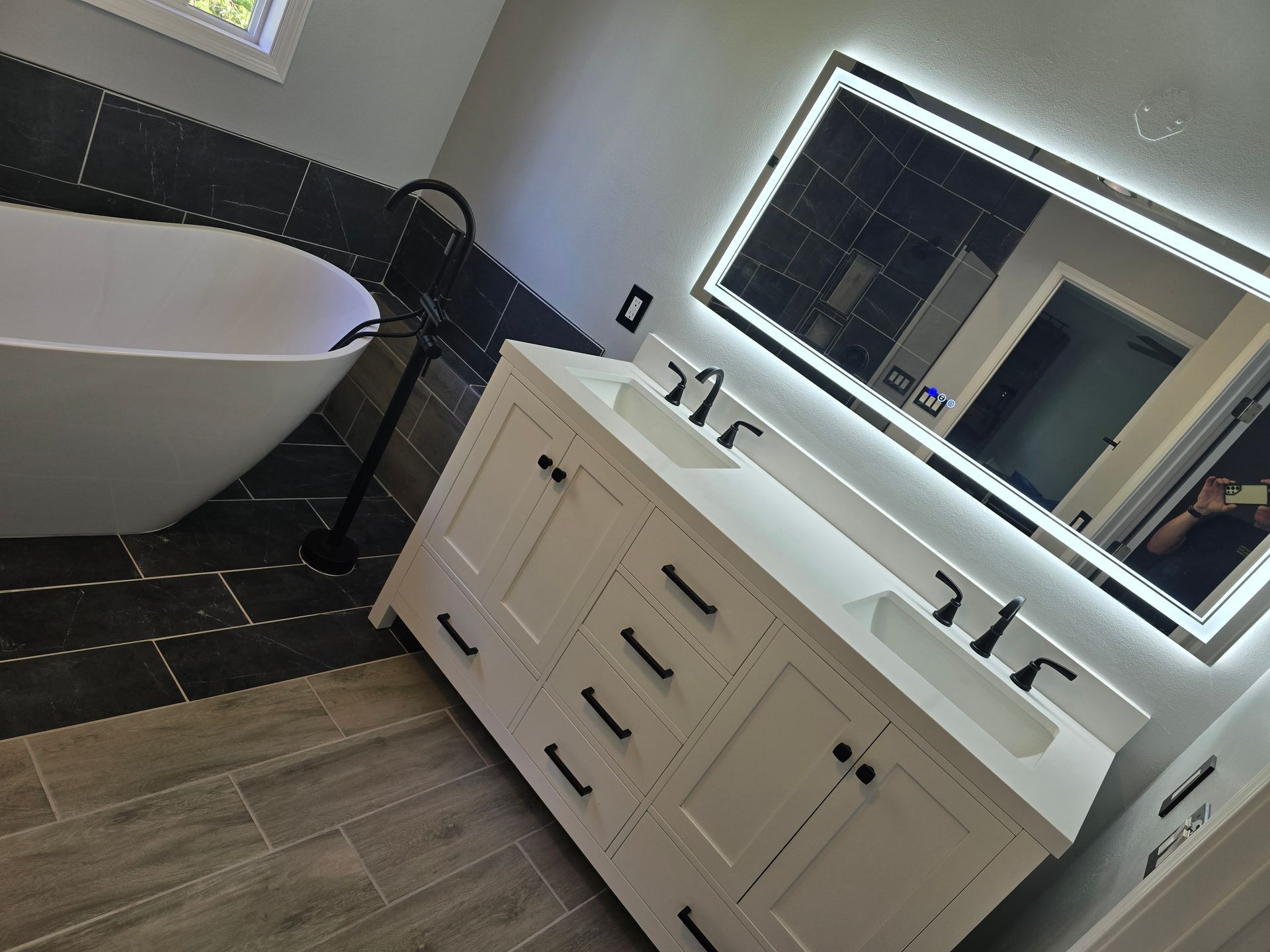 Modern bathroom with white vanity, illuminated mirror, and black accents, next to a freestanding tub.