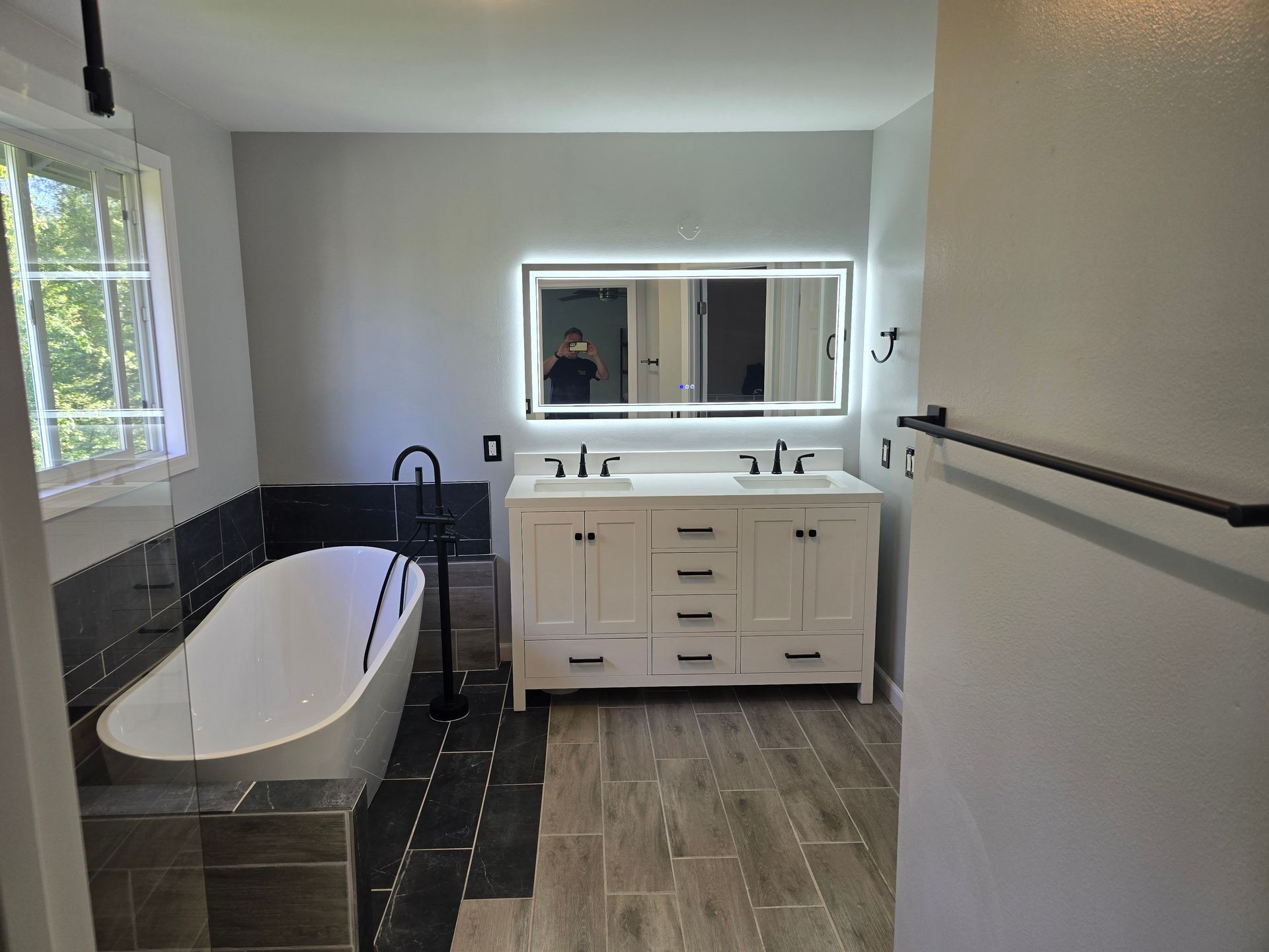 Modern bathroom with white vanity, tub, and gray tiled floor.