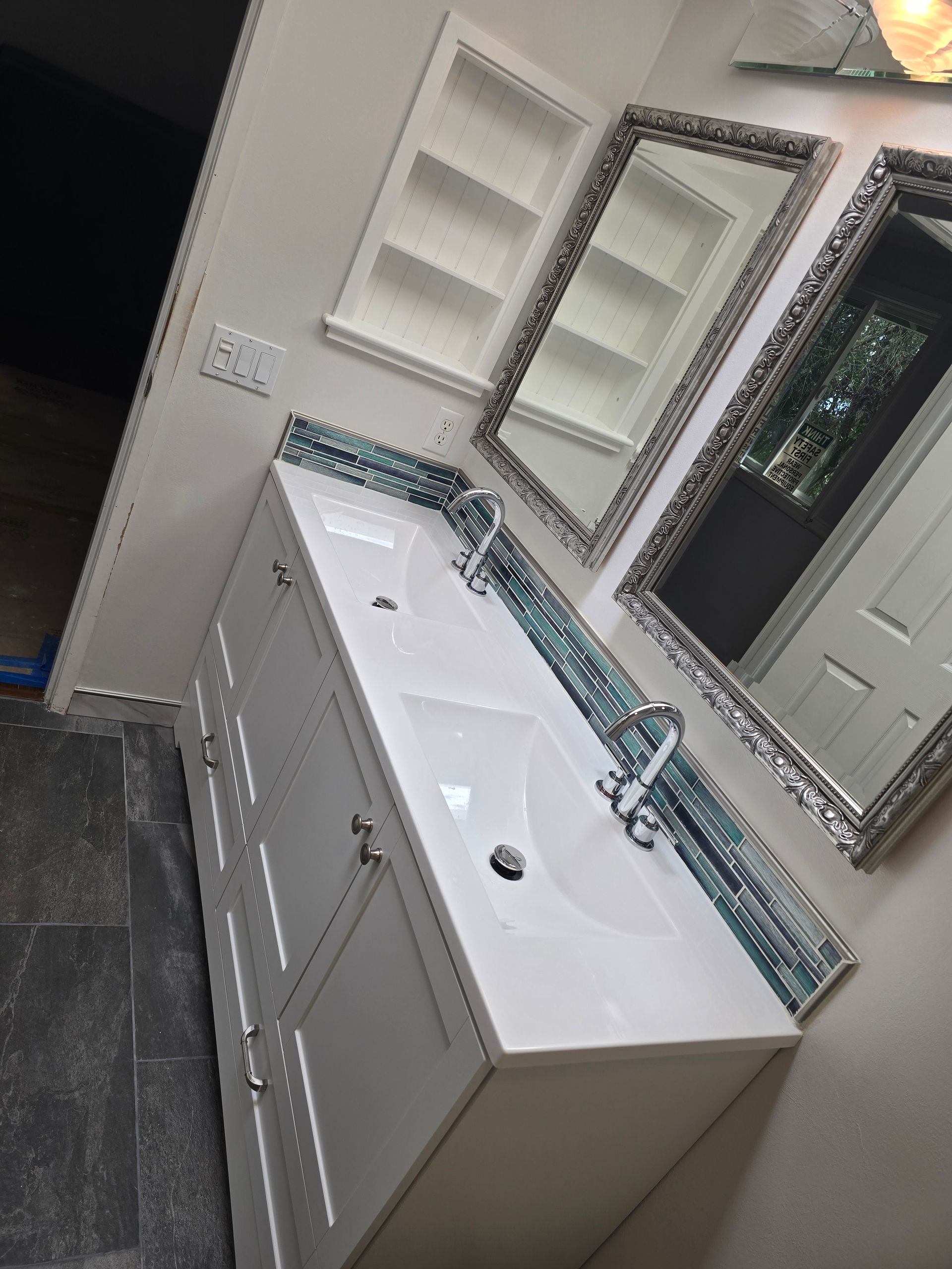 White bathroom vanity with sinks, blue tile, mirrors, and a recessed cabinet.