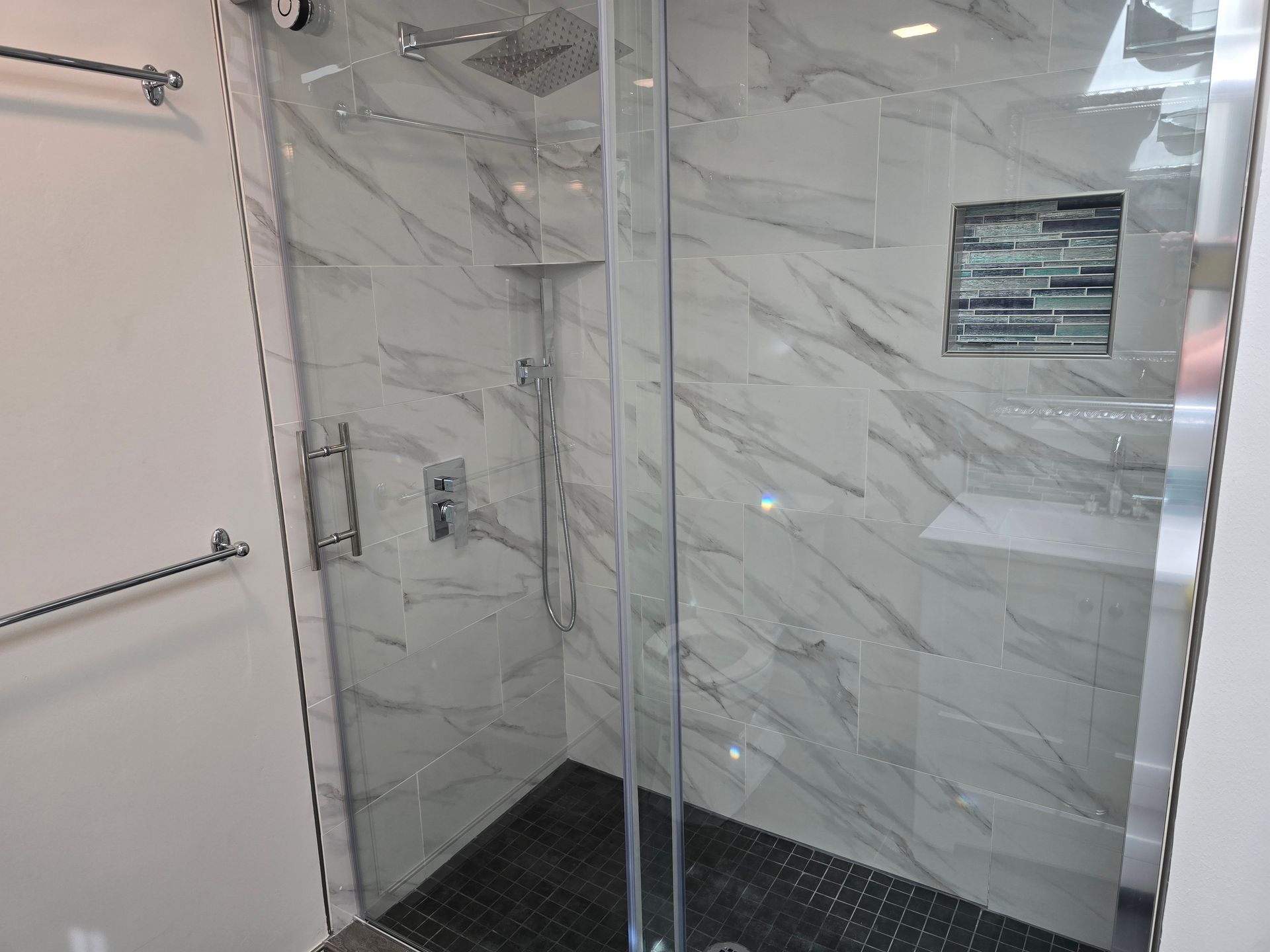 Modern shower with glass doors and marble-look tile. Silver fixtures and dark floor.