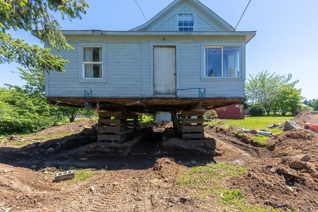 Old house raised on wooden supports in a muddy yard, possibly for foundation work.