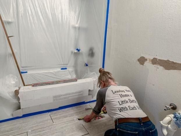 A woman is kneeling down in a bathroom while painting a bathtub.