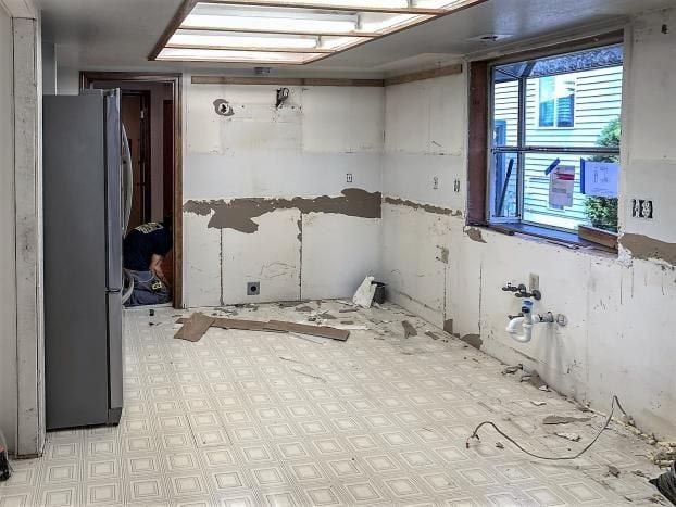 An empty kitchen with a refrigerator , sink , and window.