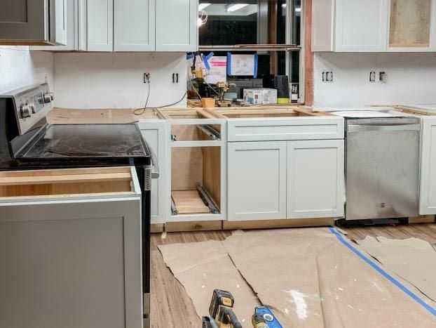 A kitchen under construction with stainless steel appliances and white cabinets.