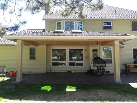 Backyard patio with a covered area attached to a yellow house. Sunny day.