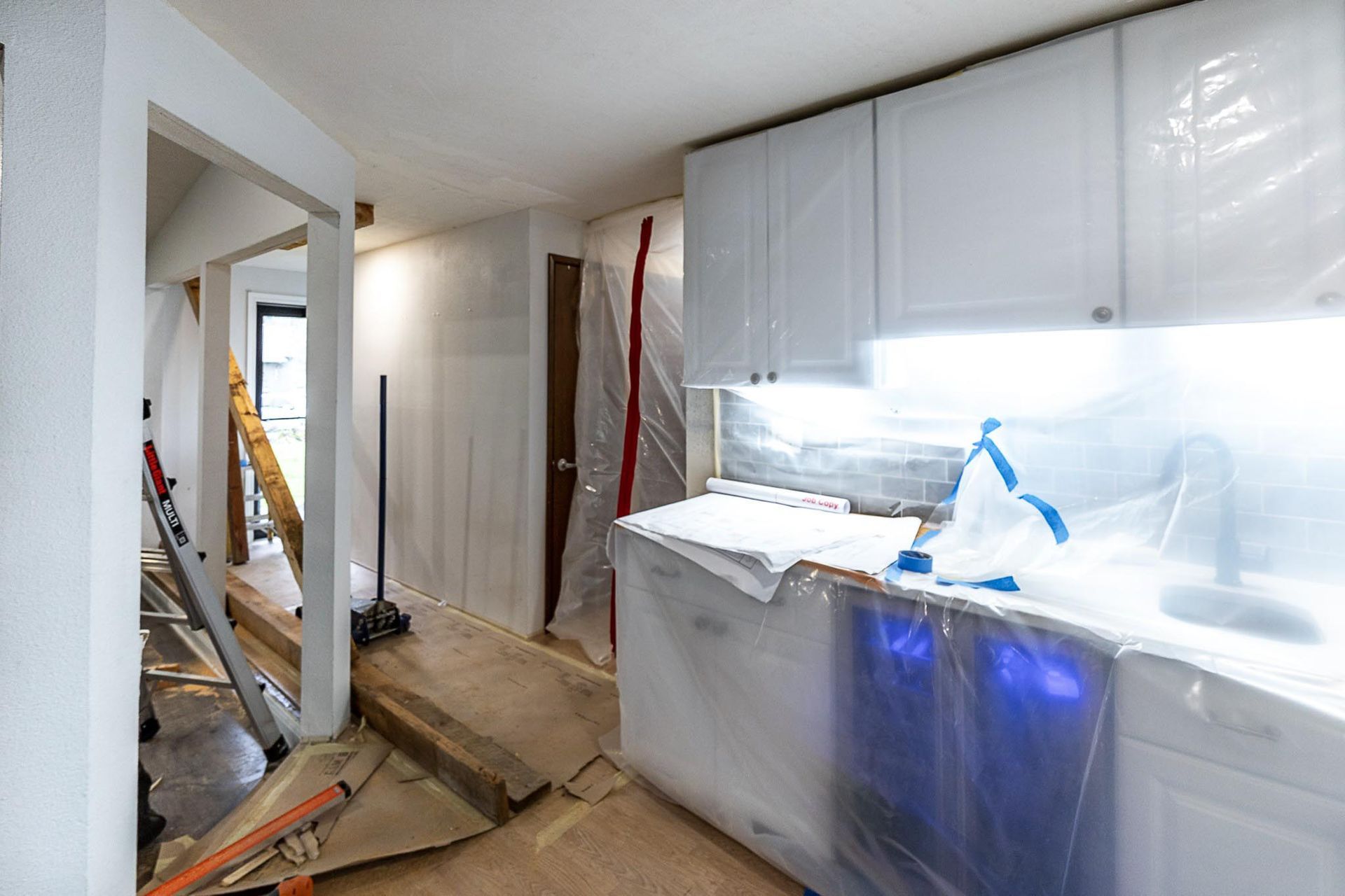 A kitchen under construction with white cabinets and a blue dishwasher.