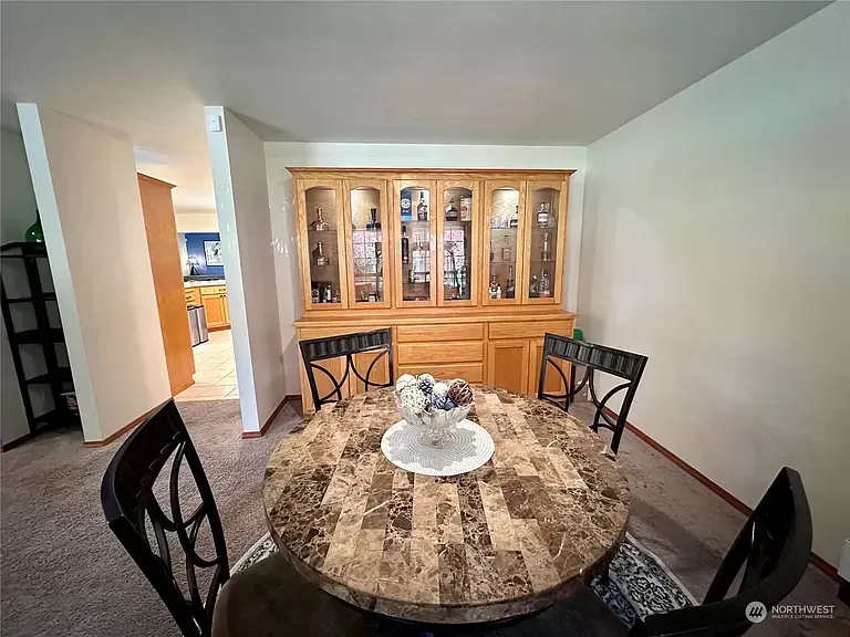 Dining room with a round table, chairs, and a wooden cabinet, looking into the kitchen.