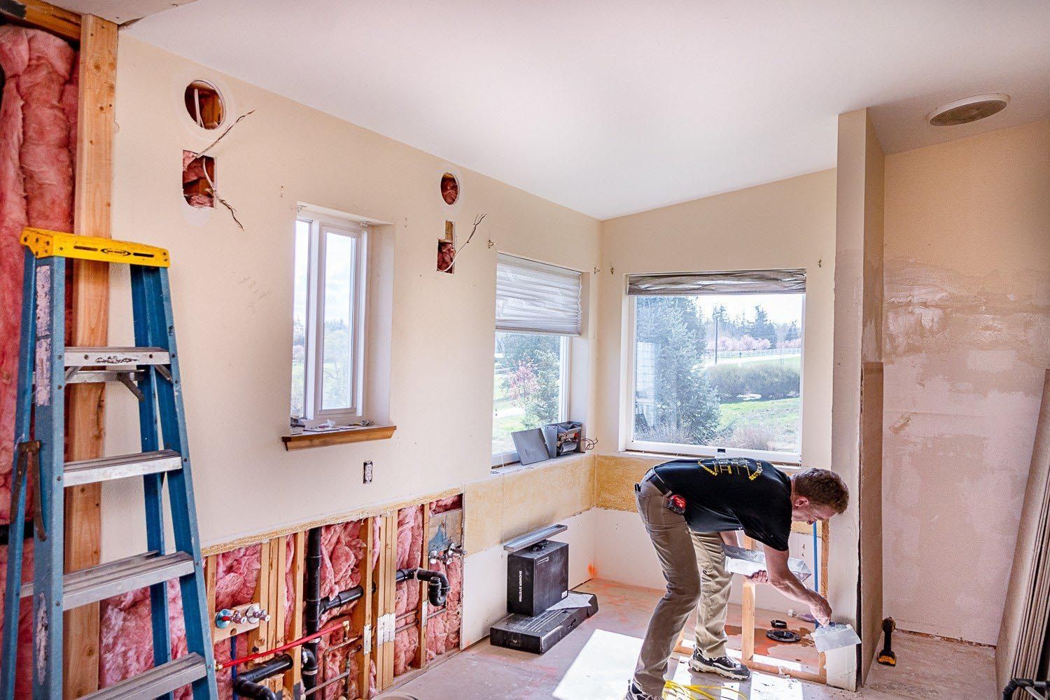 A man is working on a wall in a room with a ladder.