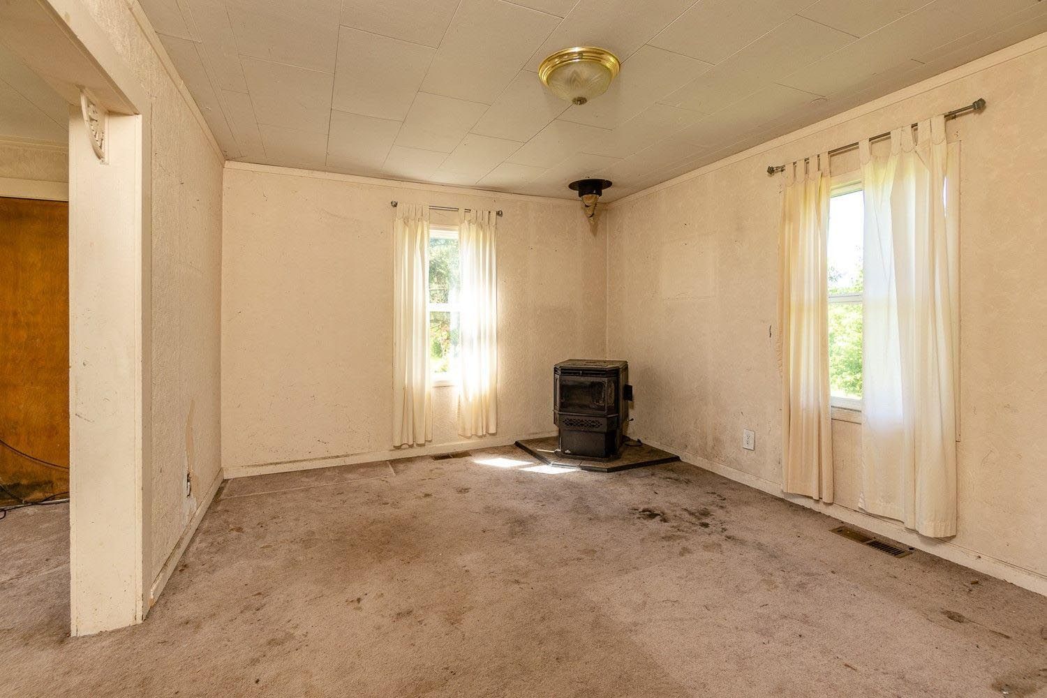 An empty living room with a stove and two windows.