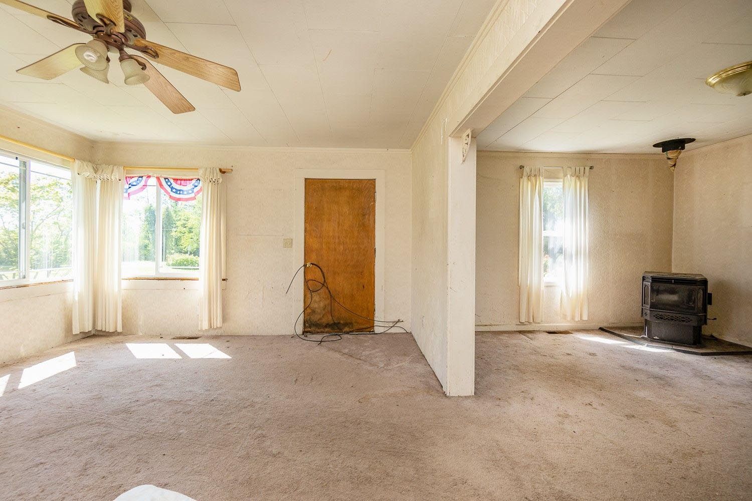 An empty living room with a ceiling fan and a wood stove.