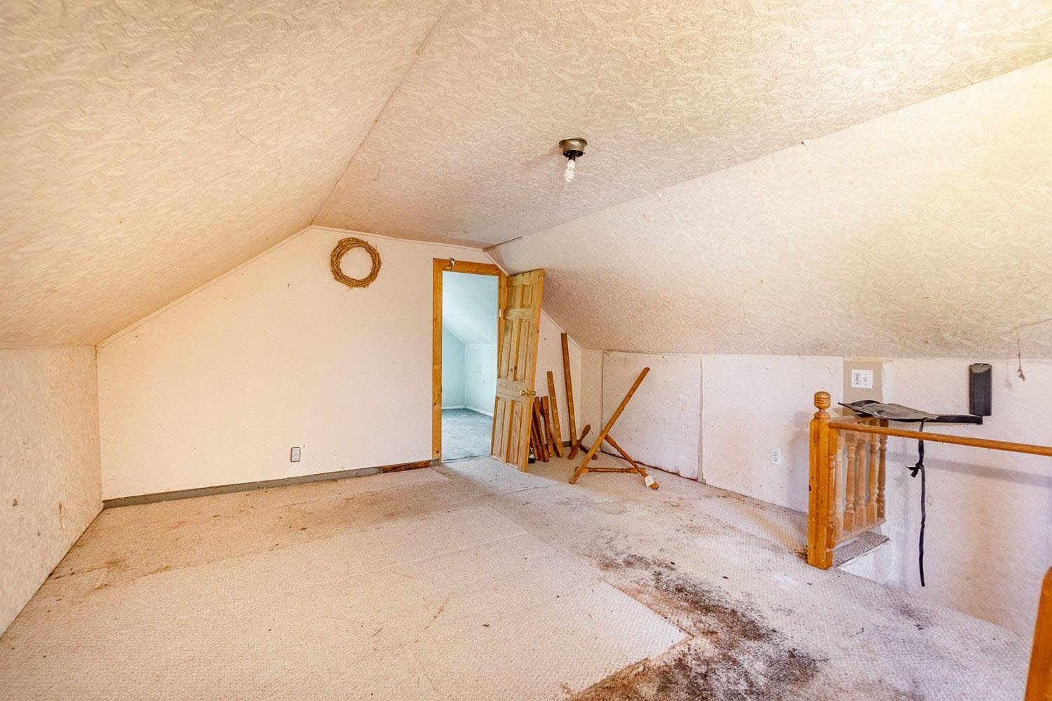 An empty attic with a staircase and a door.