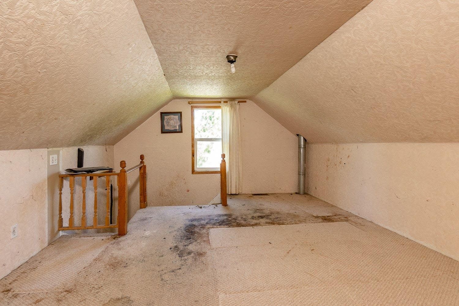 An empty attic with a carpeted floor and a window.