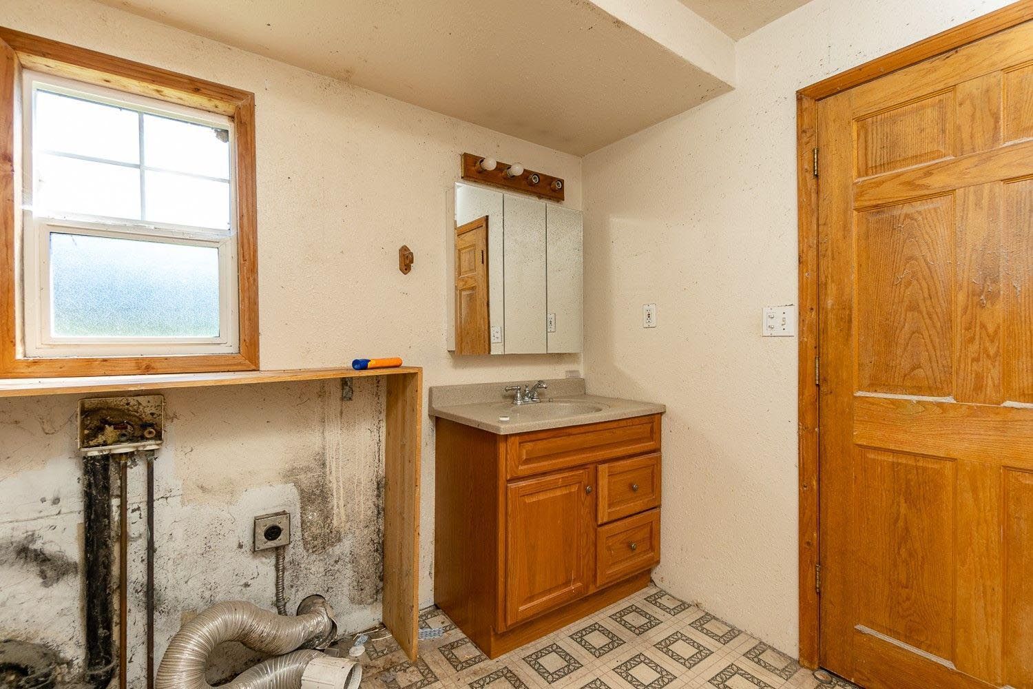 A bathroom with a sink , mirror and window.