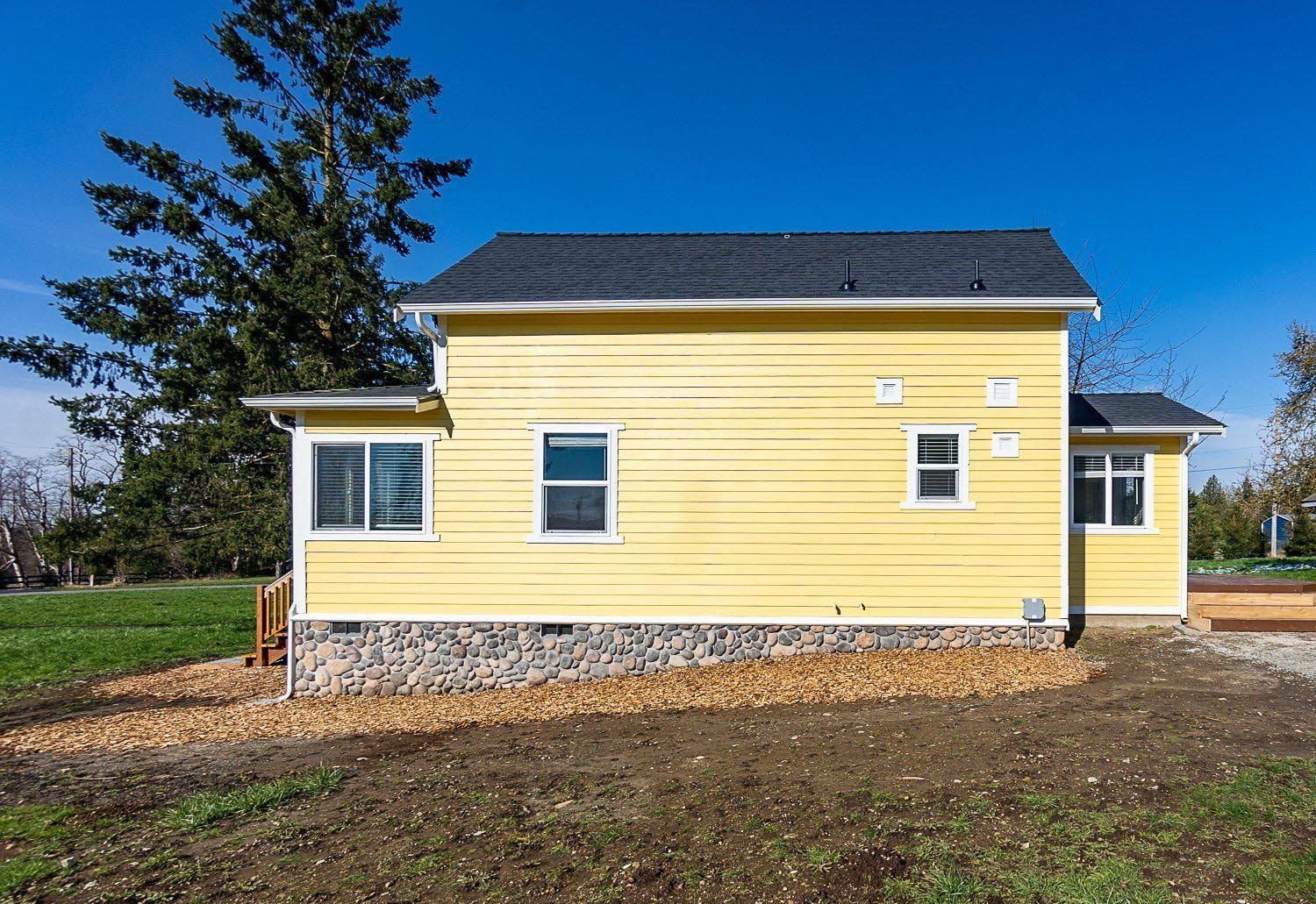 A yellow house with a black roof is sitting in the middle of a field.