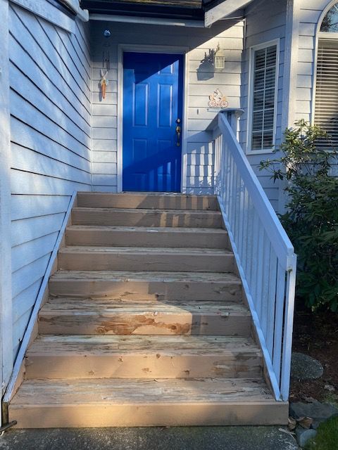 Wooden stairs leading up to a blue front door. White railing on the right. The house has blue siding.