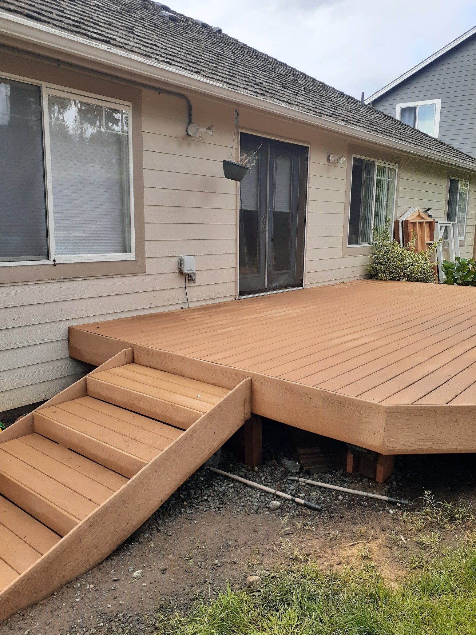 Wooden deck with stairs leading to a house with sliding glass doors and siding; green grass and gravel below.