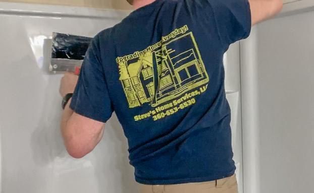 A man wearing a blue shirt with a yellow logo on the back is working on a refrigerator.