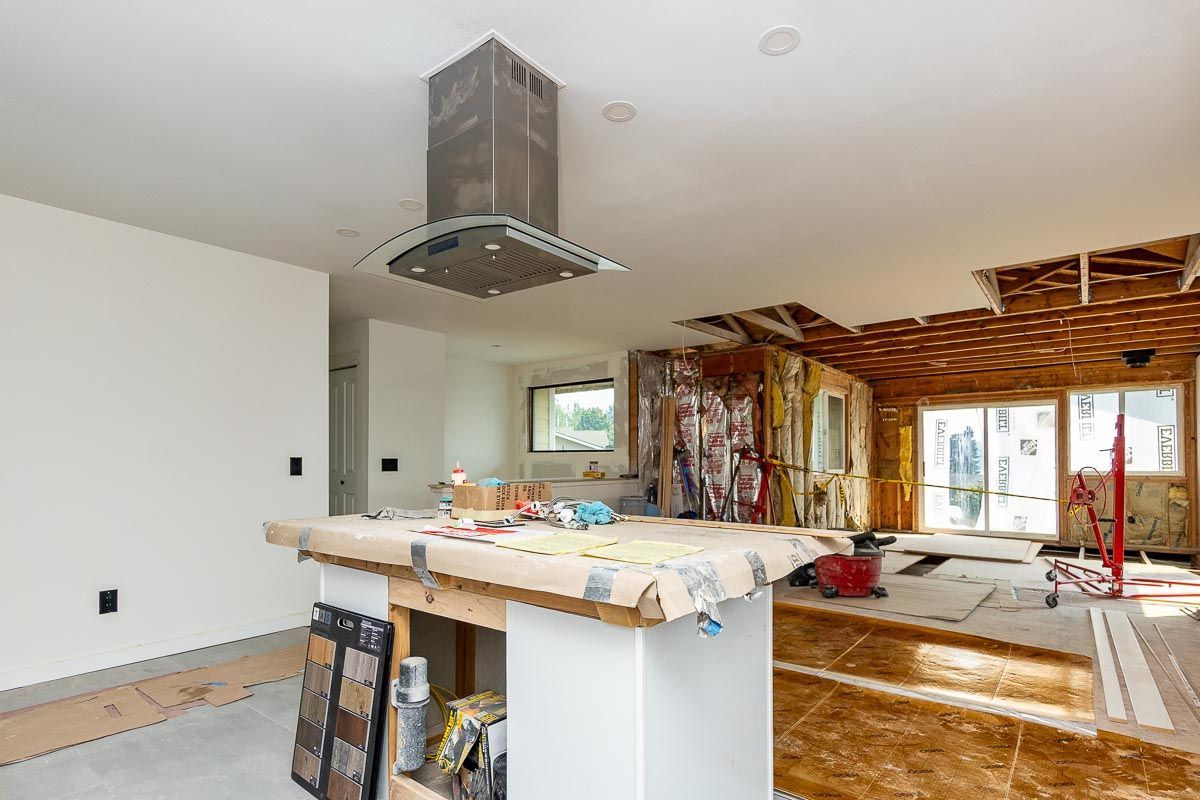 A kitchen under construction with a stainless steel hood on the ceiling.