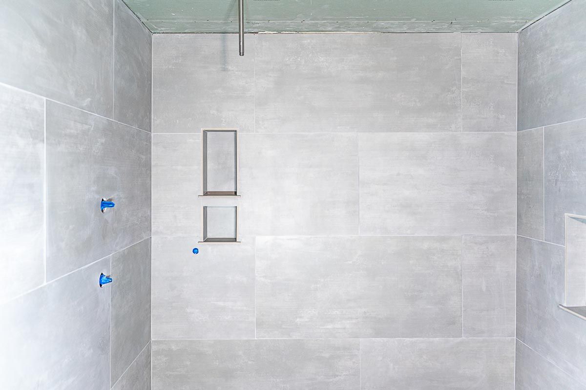 A shower stall with gray tiles and a stainless steel shower head.