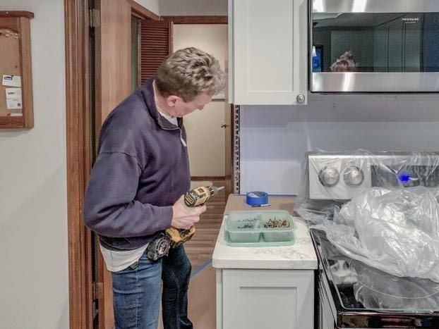 A man is standing in a kitchen holding a drill.