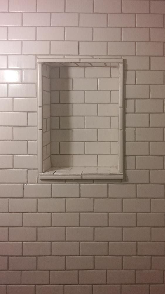 A white brick wall with a niche in the middle of it.