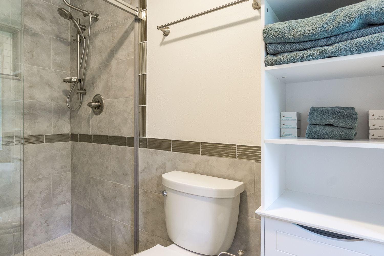A bathroom with a toilet , shower , and shelves.
