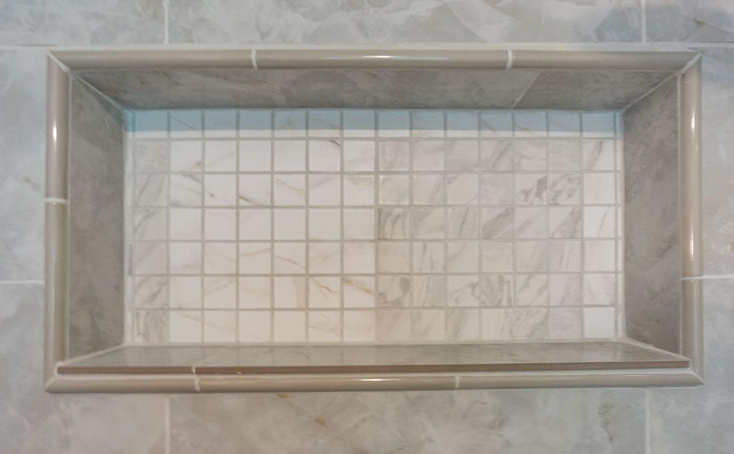 A shower niche with a tiled floor and a shelf in a bathroom.