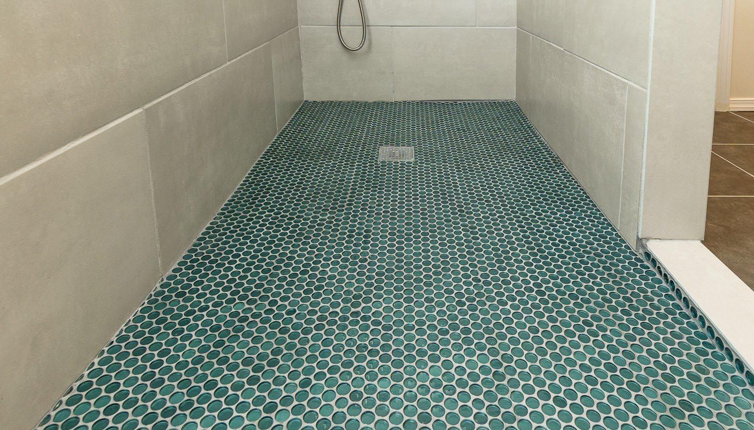 A shower stall with a green tile floor and a drain.