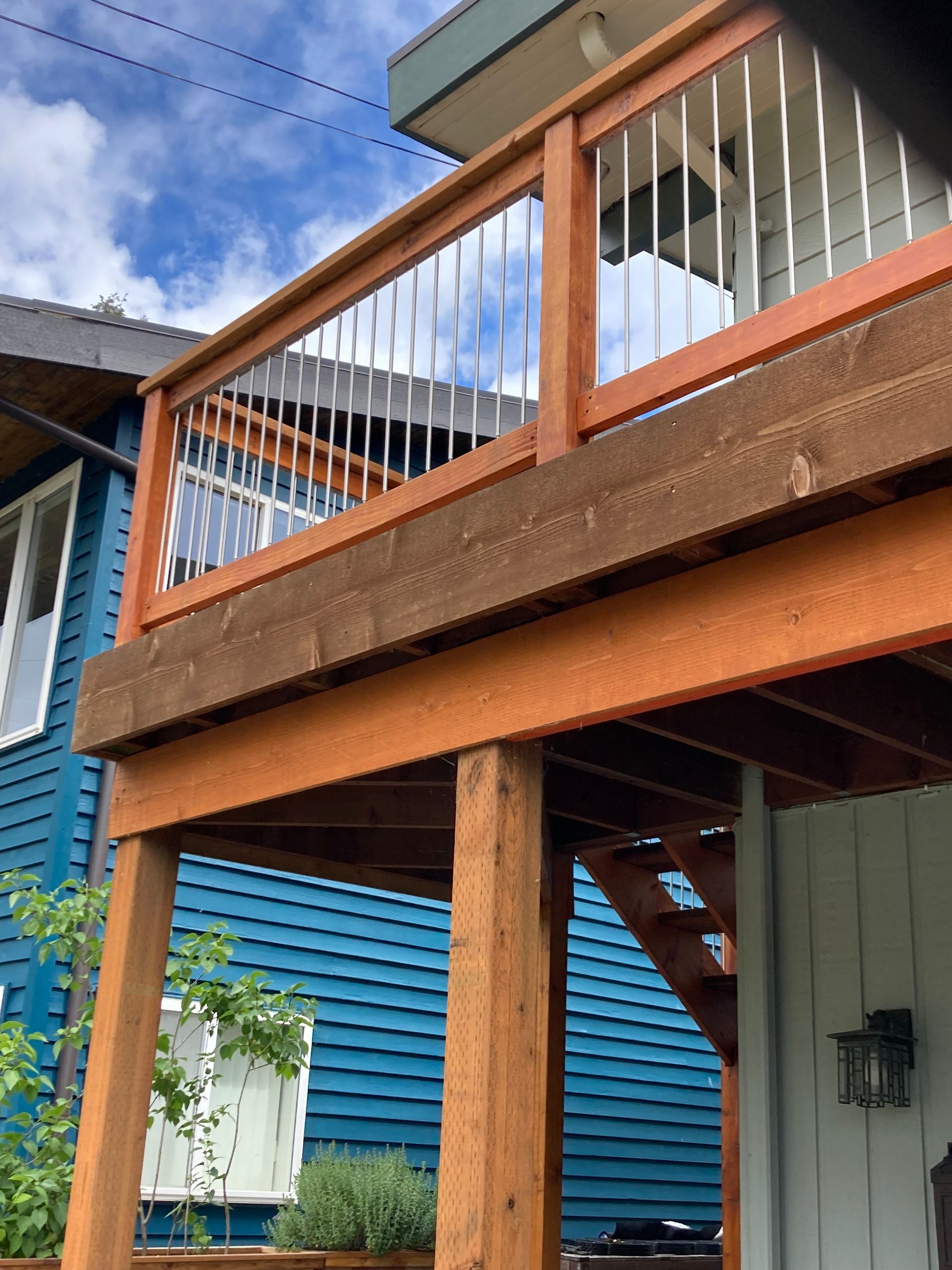 Wooden deck with metal railings, on a blue house, with a partial view of the sky.