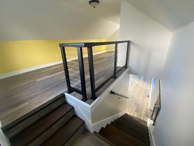 Wooden stairs leading to a loft with black railing and cable, yellow and white walls.
