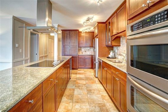 Kitchen with wood cabinets, island, and stainless steel appliances. Beige tile flooring and granite countertops.