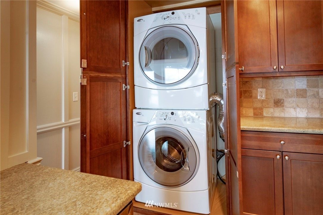 Stacked washer and dryer inside a wooden cabinet, viewed in a kitchen.